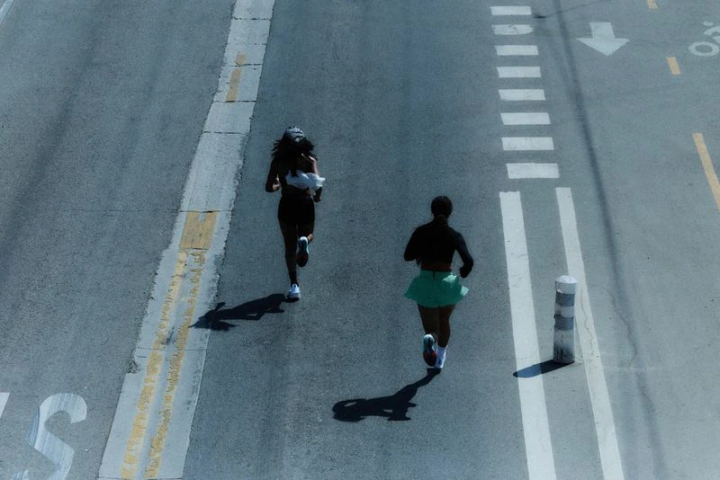 High-angle shot of two women running on a road marked with street lines and zebra crossing; fitness and urban lifestyle concept.