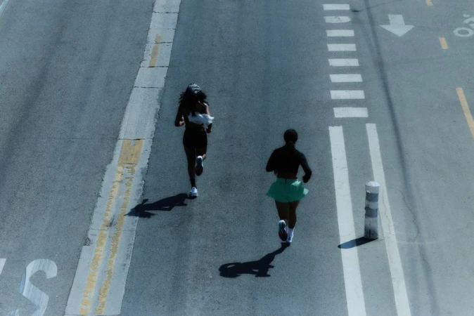 High-angle shot of two women running on a road marked with street lines and zebra crossing; fitness and urban lifestyle concept.