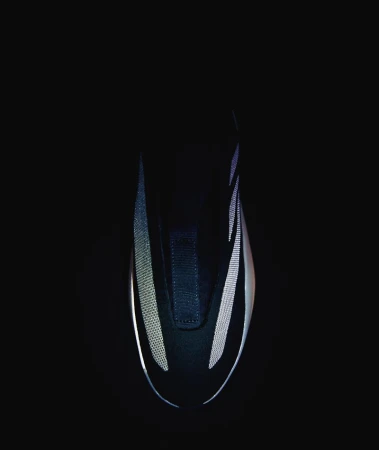 Close-up of a sleek, black shoe featuring reflective silver accents, set against a stark black background for a minimalist aesthetic.