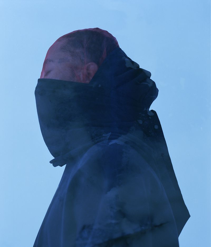 Abstract image of a person with partially covered face wearing a blue hooded garment, set against a light blue background.