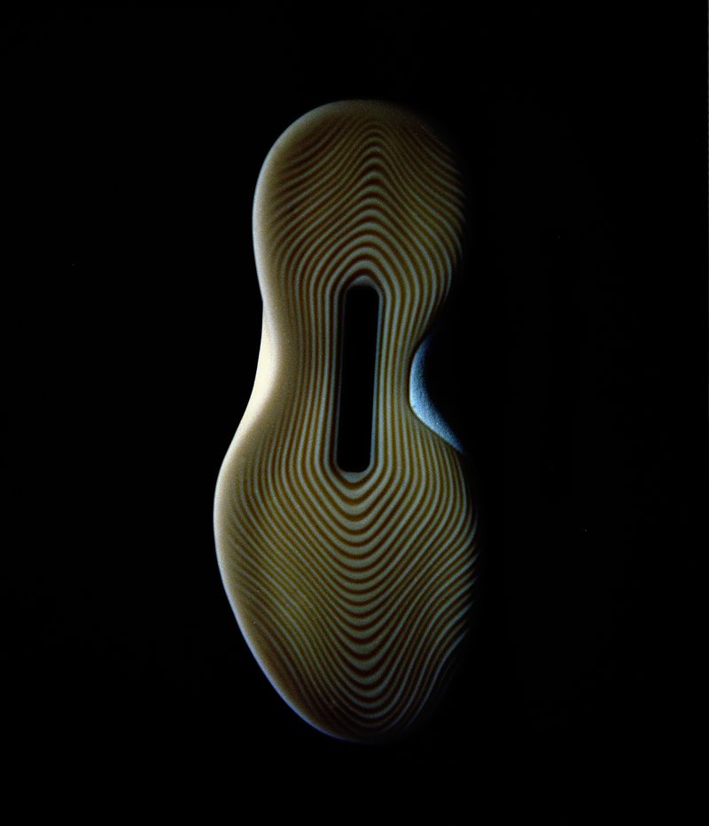 Close-up studio shot of light tan shoe sole with patterned grooves and a rectangular cutout on black backdrop with dramatic lighting.