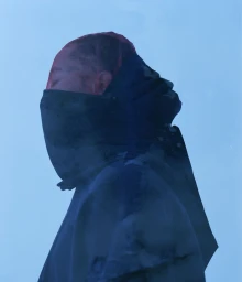 Side profile portrait of Derrick Rose wearing a high-collared dark hood and face covering bathed in cool blue light.