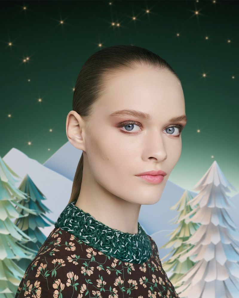 Close-up of a fair-skinned woman with light eyes and brown hair in front of a wintery green and white backdrop with twinkling stars.