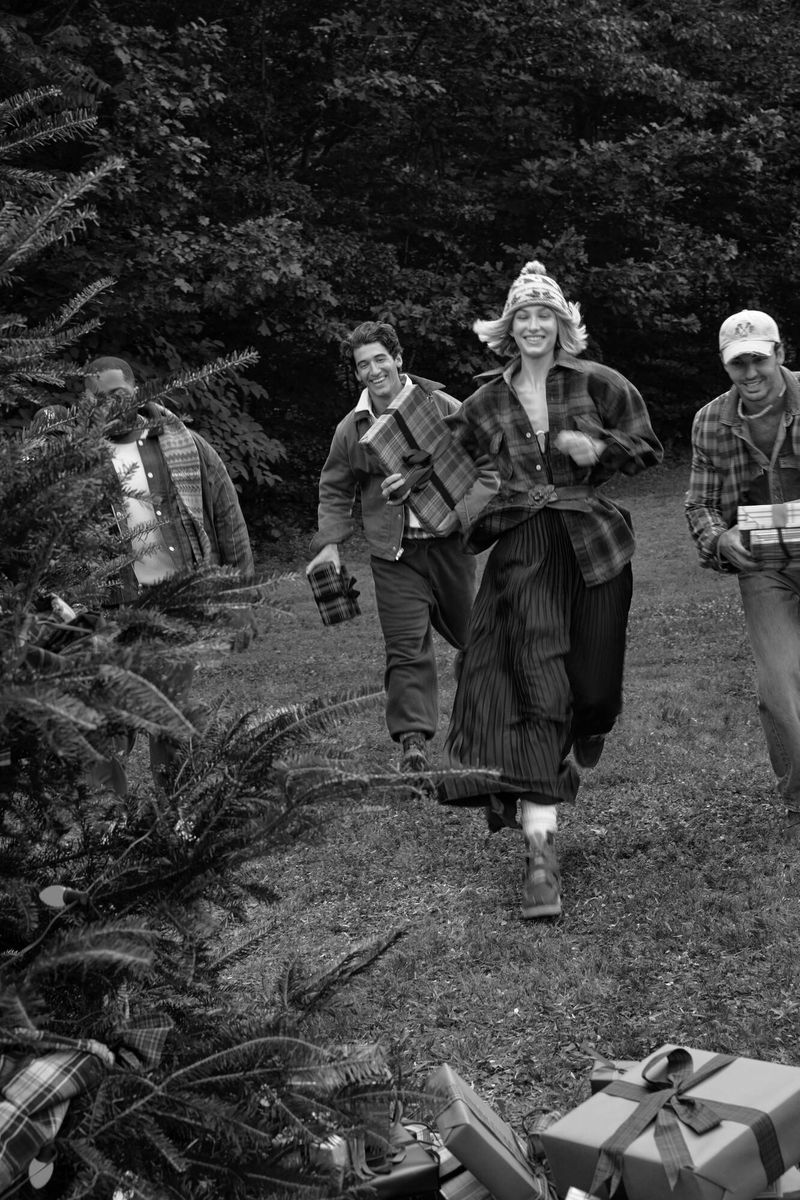 Four people running outdoors with Christmas tree and gifts. Black and white image shows them with a forest backdrop.