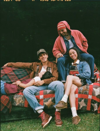 Four models relaxing together on a quilt-draped outdoor couch against dark greenery for Abercrombie & Fitch.