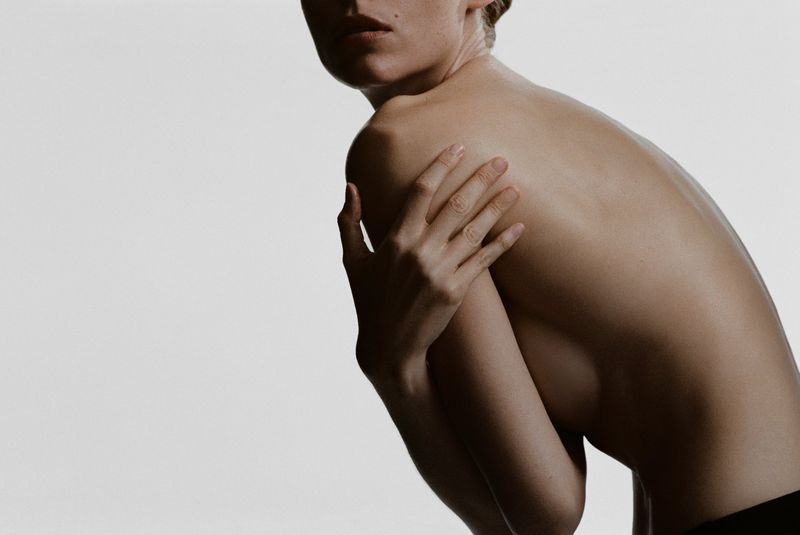 Upper torso shot of a nude adult female with fair skin, posing in a studio setting against a plain white background.
