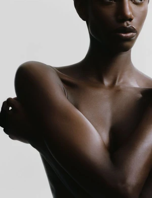 Close-up portrait of a Black woman embracing herself against a neutral light background for Necessaire.