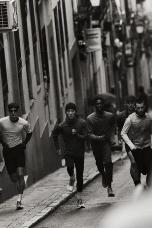 Black and white photo of male runners including Hyuk Kim sprinting down a narrow urban street in technical running apparel.