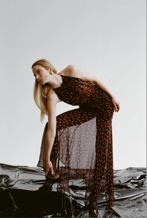 Model Eniko Mihalik wearing a sheer polka dot halter jumpsuit against a white seamless backdrop