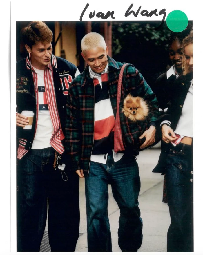 Model Ivan Wang walking down a city street carrying a small dog in a plaid bag alongside friends in Tommy Jeans apparel.
