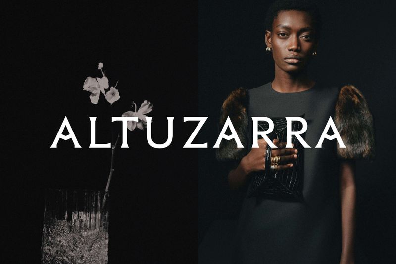 Fashion shot of a Black woman in dress with fur sleeves, holding a black purse, against a dark backdrop. 'Altuzarra' text overlay.