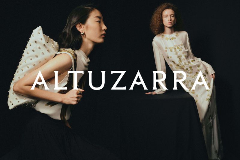 Two women pose in a fashion shot against a dark background, featuring Altuzarra logo in the foreground. One wears a dress, the other wears a studded bag.