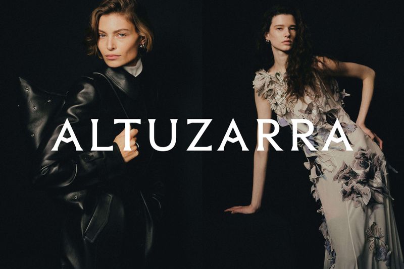 Two women pose against a dark backdrop showcasing Altuzarra fashion: one in a leather jacket and the other in a floral gown.