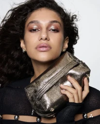 Model with dark curly hair holding a textured metallic handbag against a plain white background