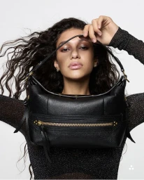 Model Tamar David holding a black textured leather shoulder bag framed in front of her face against a white studio background.