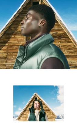 Close-up portrait of a Black man wearing a green puffer vest with his eyes closed outdoors in front of a wooden cabin.