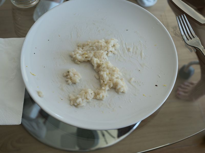 Rice shaped like Italy on a white plate, top-down view, suggesting Italian cuisine and creative food presentation on a neutral background.