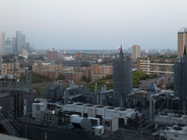 Aerial view of a cityscape featuring dense buildings, industrial rooftop structures, and high-rise skyscrapers in the hazy distance.