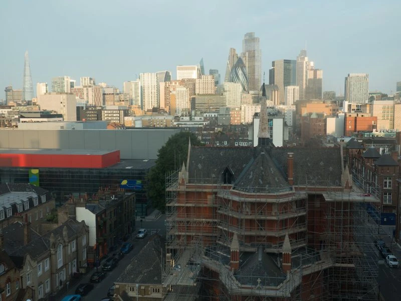 Cityscape view of London featuring modern buildings, traditional architecture, and scaffolding, under a bright, hazy sky.