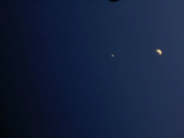 A glowing crescent moon and a single bright star shine against a vast, deep dark navy blue evening sky.