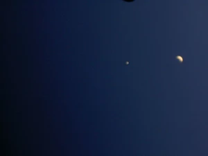 A glowing crescent moon and a single bright star shine against a vast, deep dark navy blue evening sky.