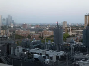 High-angle view of industrial rooftop machinery and ventilation units overlooking an urban cityscape under an overcast sky.