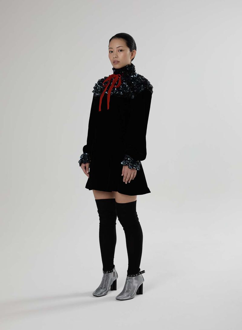 A young Asian woman models a black velvet mini dress with embellishments, paired with thigh-high socks and silver ankle boots on a white background.