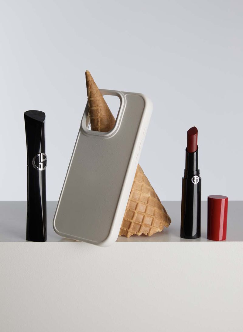 Still life of Armani beauty products including lipstick and mascara next to a grey mobile phone case and an ice cream cone.