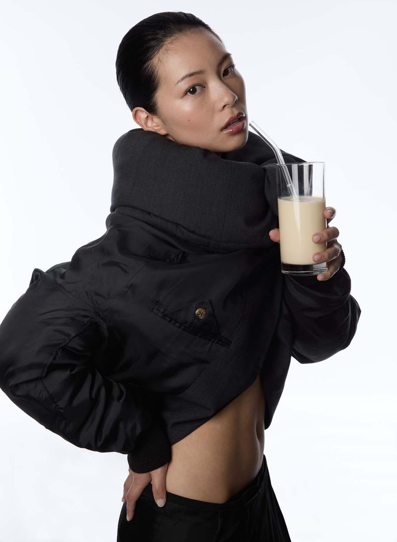 Model Ting Ting Lai in a cropped black bomber jacket holding a glass of iced beverage against a white background.