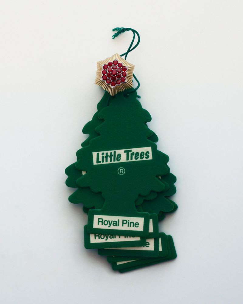 Close-up of a stack of green Little Trees air fresheners in the shape of a Christmas tree with "Royal Pine" text, with a jeweled broach.