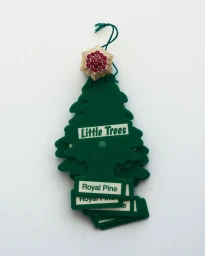 Van Cleef & Arpels gold ruby ring resting on top of stacked green pine tree car air fresheners against a white background.