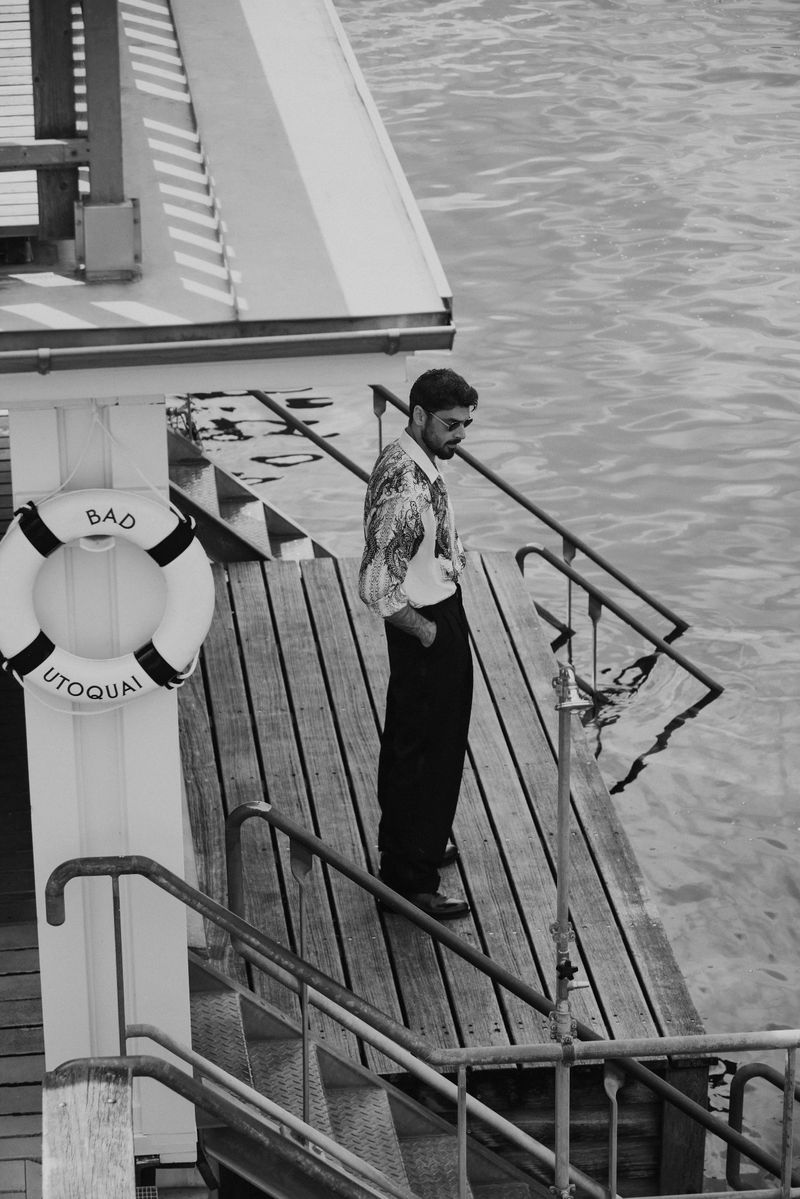 Black and white photo of a man standing on a wooden dock with a life preserver and stairs leading to the water.