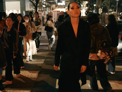 Model in black blazer walking through a crowded street at night for Carpark Magazine 19 in Seoul.