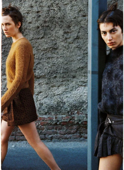 Two models in fuzzy knit sweaters and mini skirts posed outdoors by a textured wall for Vogue Portugal.