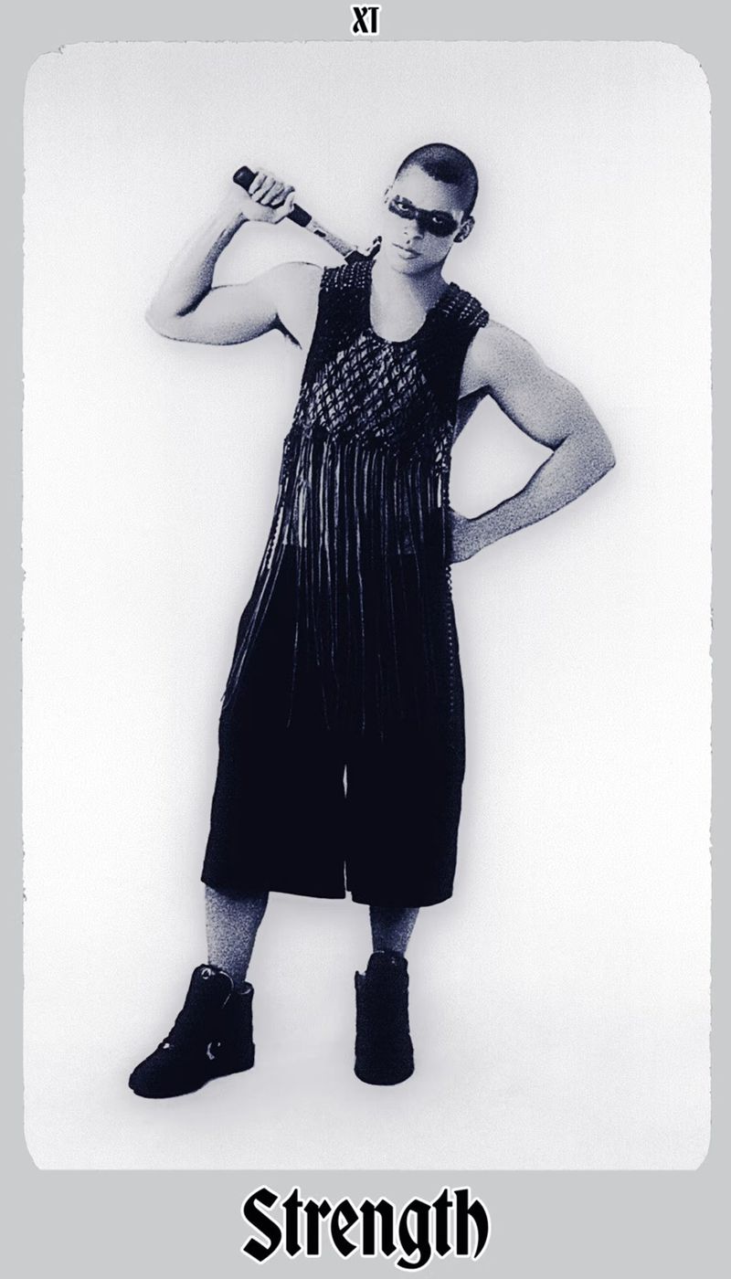 Monochrome portrait of a muscular adult male in alternative fashion holding a baton-like object, styled in a tarot card format.