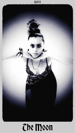 Monochrome tarot card image featuring a woman with a high bun, adorned with necklaces, posing with outstretched arms in a studio setting.
