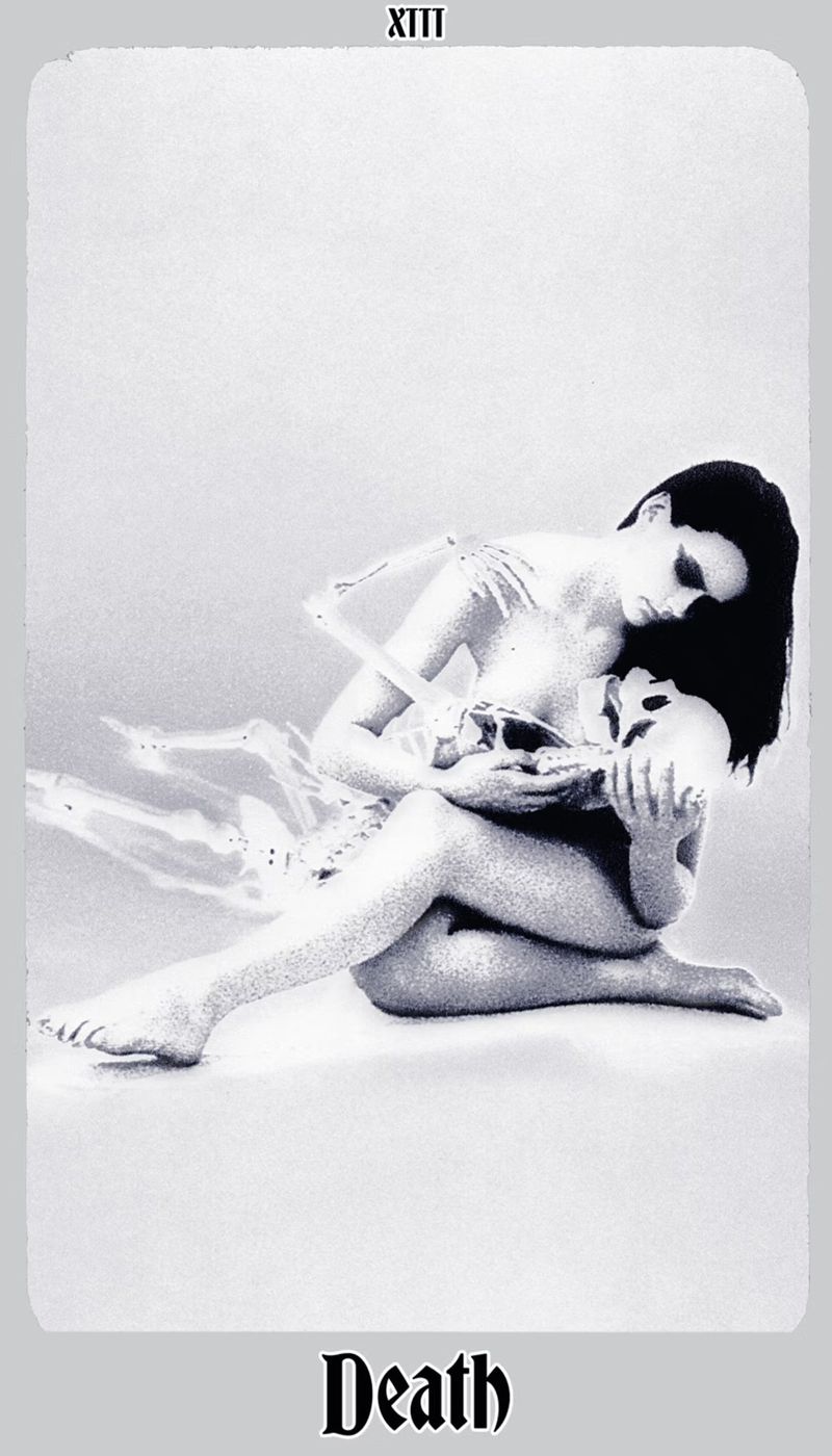 Artistic grayscale image featuring a seated woman tenderly holding a skull and embracing a skeleton torso, reminiscent of tarot card imagery.