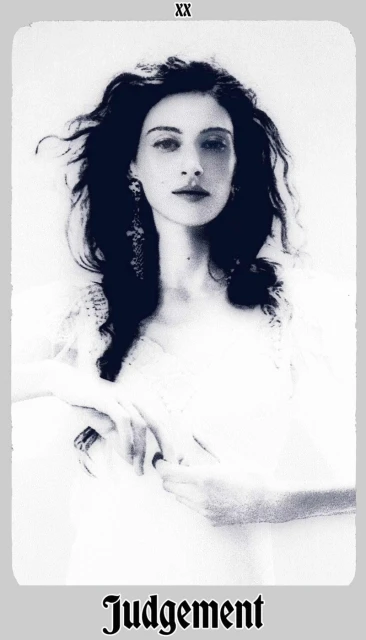 Black and white portrait of a woman with long dark hair, wearing earrings, and white clothing, set against a bright, soft background.