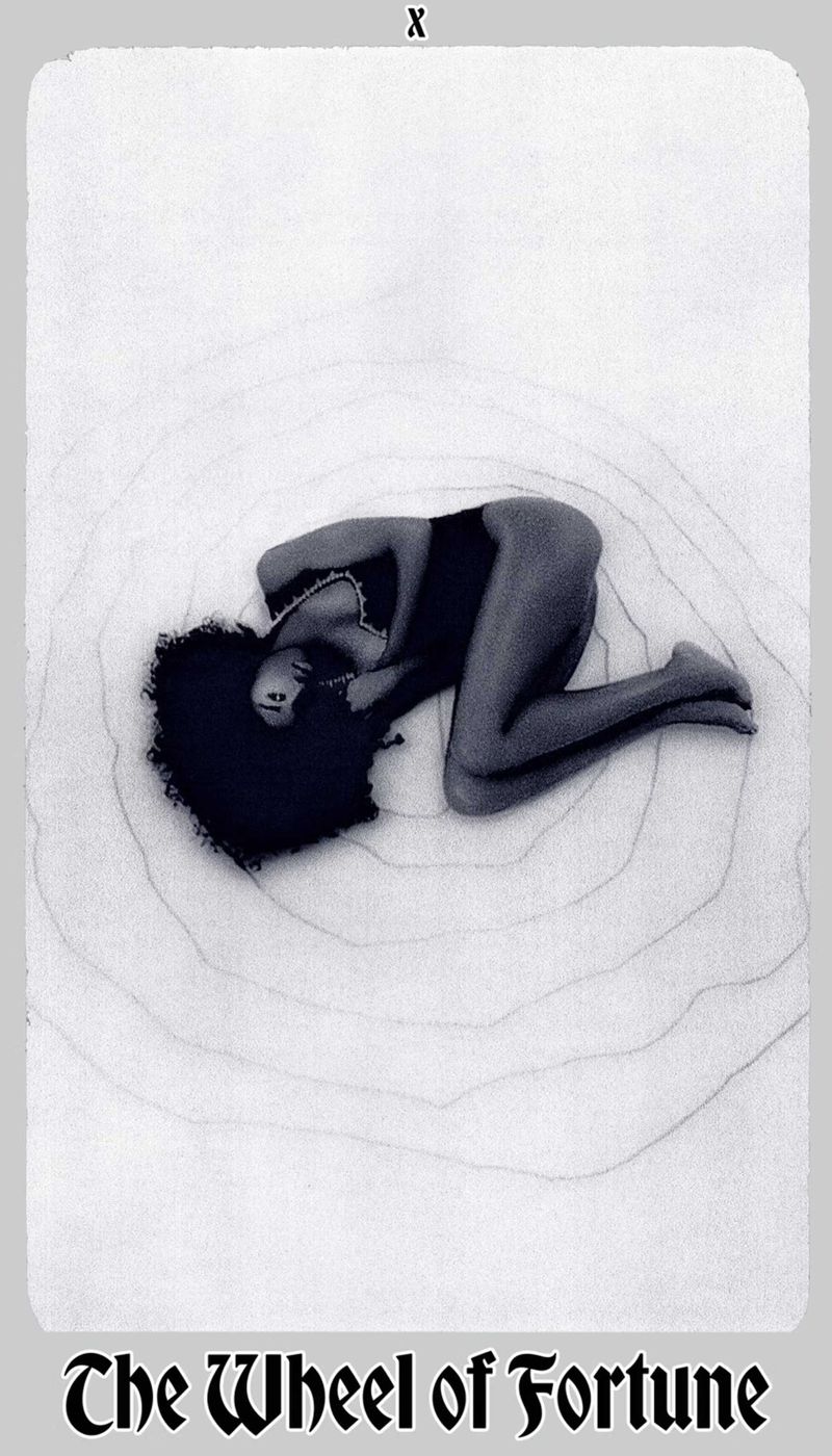 Monochrome image of a woman with afro lying on a surface with concentric circle patterns, resembling a tarot card aesthetic.