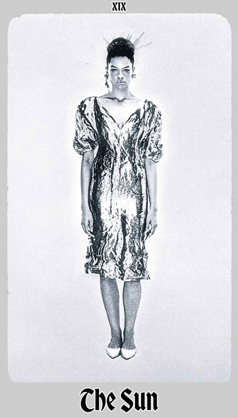 Full-length studio shot of a woman in a shimmering silver dress, with hair styled up and white shoes, against a white background.