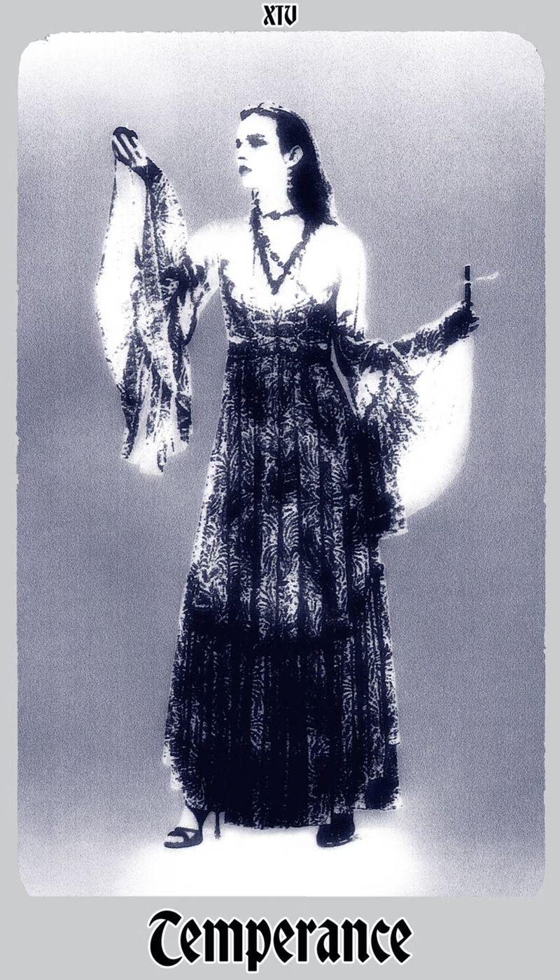 Monochromatic studio shot of a woman in an elegant dress, holding objects, against a glowing backdrop, portraying a tarot card theme.