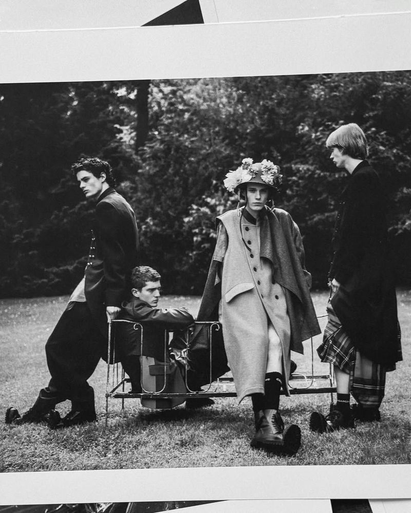 Black and white outdoor fashion photo featuring four young adult models posing near foliage and an iron bench seat.