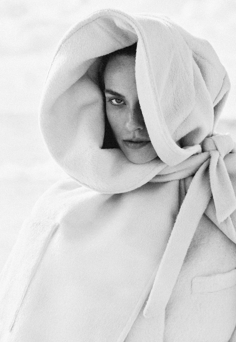 Black and white portrait of a woman framed closely inside an oversized white hooded cape with a neck tie.