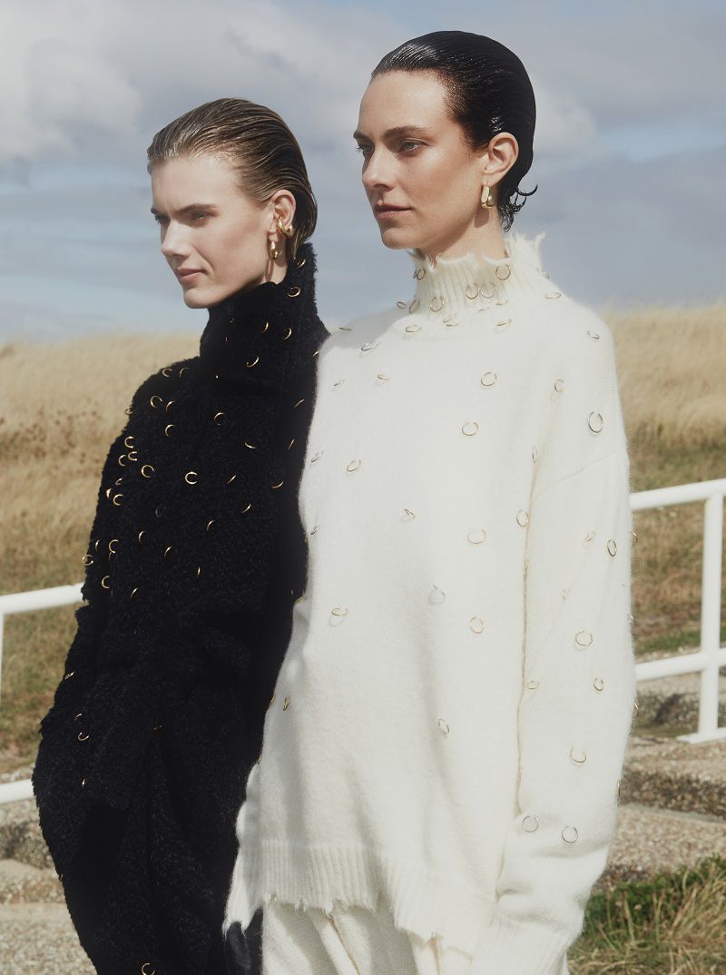 Two models in embellished black and cream knit sweaters outdoors with slicked-back hair.