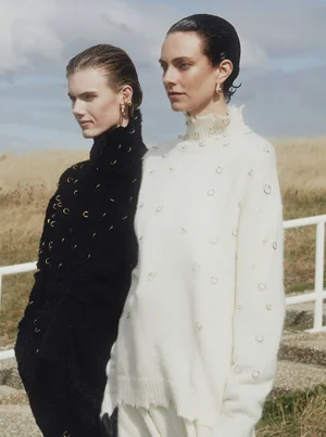 Two models in embellished black and cream knit sweaters outdoors with slicked-back hair.