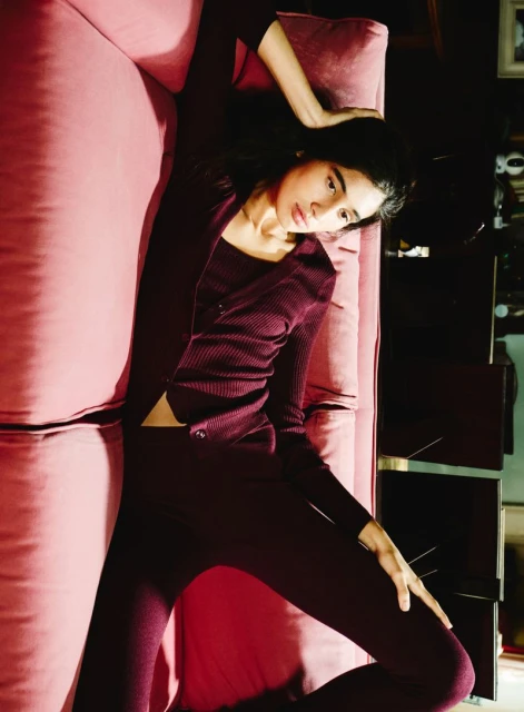 Woman in a maroon cardigan, top, and leggings lying on a pink couch. Fashion shot with a dark, classy, and modern design aesthetic.
