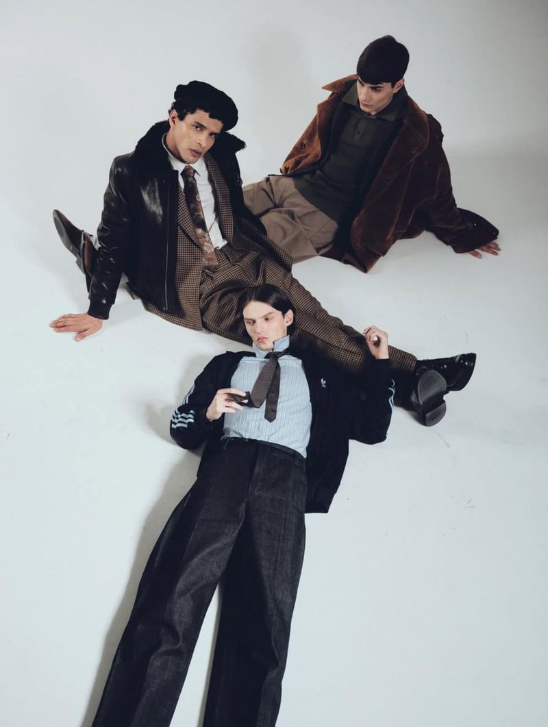 Three men in fashionable vintage-inspired outerwear lying on a white surface, showcasing retro menswear fashion with coordinated styling and design.