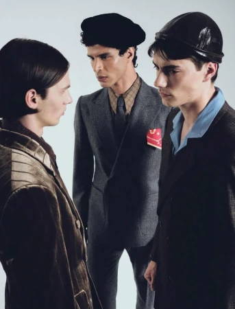 Three male models in tailored suits, beret, and cap posing against a pale studio backdrop in an editorial composition.