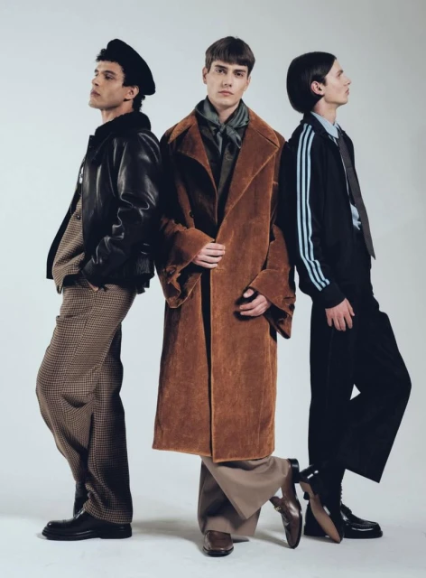 Three male fashion models strike a pose indoors against a clean white background, showcasing an array of jackets, pants, and footwear.