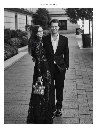 Monochrome portrait of a stylish couple outdoors with building backdrop. The woman has a sequined gown and purse. The man wears a suit.
